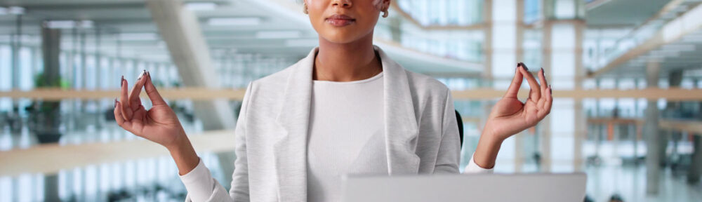 stress-relief | Professional woman practicing mindfulness meditation at office desk with laptop, demonstrating stress management techniques for paralegals